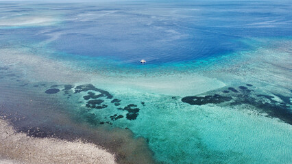 A solo motorboat on the edge of a stunning coral reef on turquoise and blue ocean on tropical Atauro Island Timor Leste, aerial drone