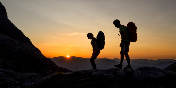 Silhouette of couple with backpack walking on mountain at sunset