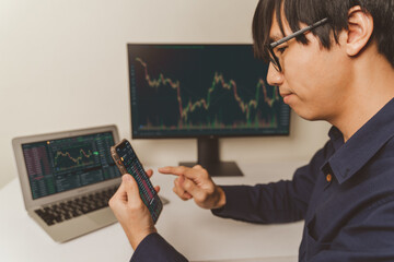 Young business Trader, investor or businessman is pointing on smartphone, laptop on trading stock market graph, candlestick chart as Bitcoin Cryptocurrency price chart. Investing money trader concept