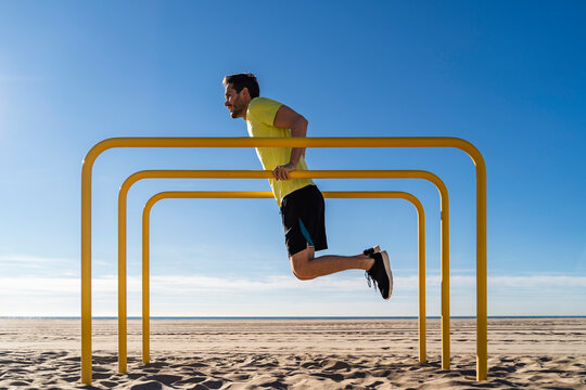 Athlete doing push ups on parallel bars at beach