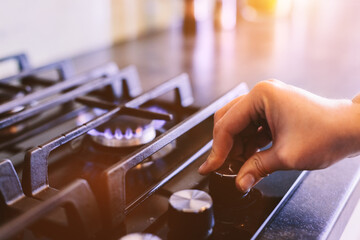 Hand turning on gas burner on kitchen stove top - obrazy, fototapety, plakaty