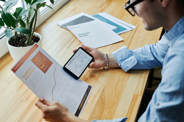 Businessman comparing cryptocurrency data through smart phone at office