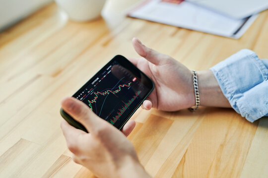 Businessman holding smart phone on desk with cryptocurrency trading graph at office