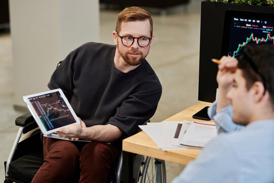 Disabled businessman showing cryptocurrency graph on tablet PC to colleague in office