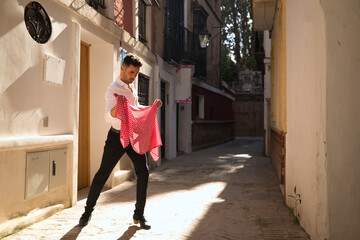 Young Spanish man in white shirt and black pants and dance shoes, dancing flamenco with a red...