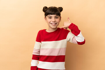 Little caucasian girl isolated on beige background making phone gesture. Call me back sign