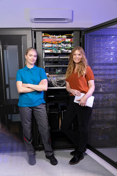 Smiling technician and trainee standing together in server room
