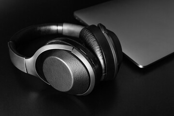 close-up of wireless headphones and laptop on black background, table. Music online enjoy listening. Concept coworking, workplace, harmony job, lifestyle.