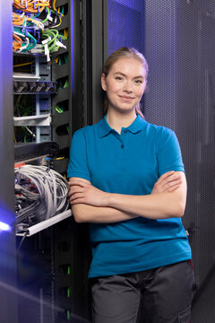 Smiling blond IT trainee standing with arms crossed in server room at industry