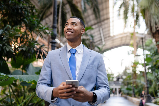 Smiling businessman with smart phone standing by plants