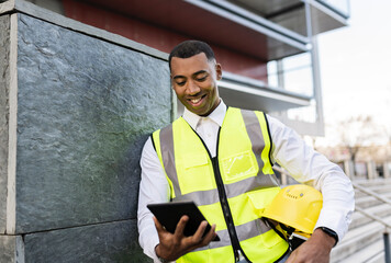 Happy architect with hardhat using tablet PC by wall