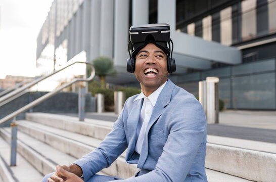 Cheerful businessman wearing virtual reality simulator sitting in front of building