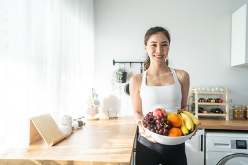 Obraz na płótnie Canvas Asian attractive active woman holding bowl of fruit in kitchen at home. 
