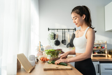 Asaian attractive woman wear sport clothes cook green salad in kitchen.