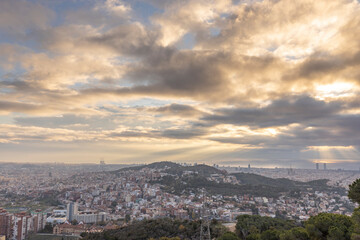 Fototapeta na wymiar Picturesque landscape of Barcelona from the hill in the early morning. Sunbeams through the clouds. Dramatic sky over the city. Autumn in Barcelona, Spain.