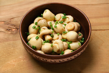 mushrooms with green onions in a clay plate, pickled champignons, one object on a wooden background