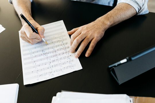 Musician writing musical notes by tablet PC at table
