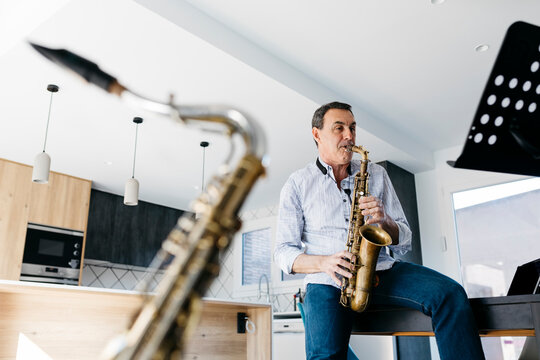 Saxophonist playing saxophone sitting on table at home