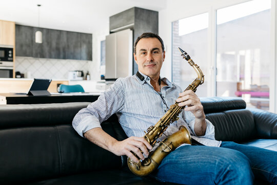 Smiling musician with saxophone sitting on sofa in living room at home