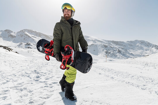 Happy young man walking with snowboard on sunny day