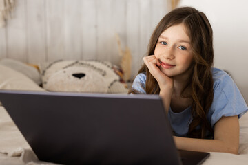 beautiful young girl lies on the bed with a laptop