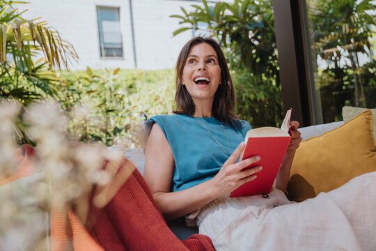 Cheerful woman with book sitting on sofa in back yard