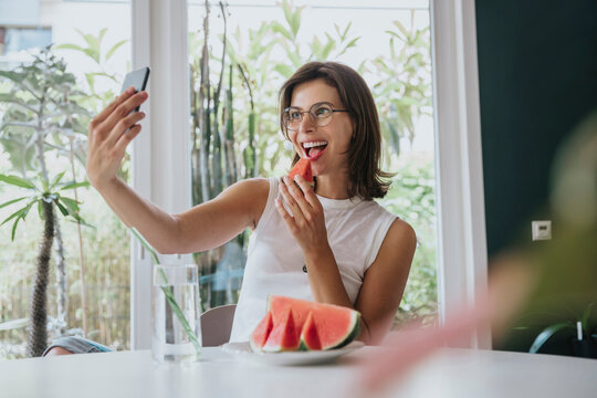 Woman taking selfie eating watermelon sitting at home