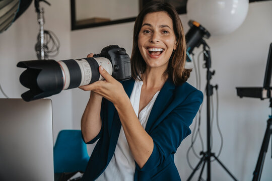 Cheerful photographer holding digital camera in studio