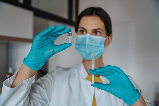 Female doctor holding syringe looking at vial in clinic