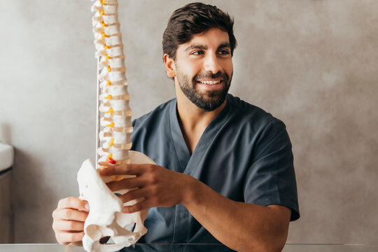 Smiling young physiotherapist with human spine model at medical clinic