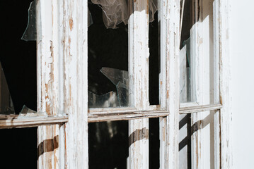 Close-up broken glass window wooden frame with cracked paint outdoors, side view