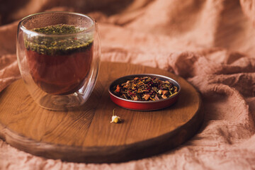A glass cup of fragrant herbal black tea on a wooden board next to scattered dry tea. Brew tea.