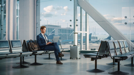 Modern Airport Terminal: Handsome Businessman Working on Laptop Computer While Waiting for His...