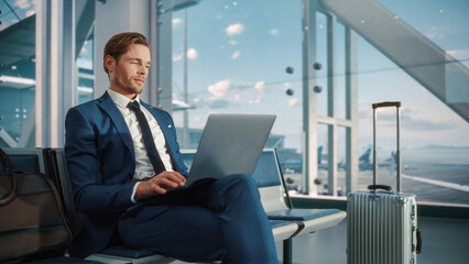 Busy Crowded Airport Terminal: Businessman Uses Laptop, Waiting for a Flight. Traveling Entrepreneur Working Online On Computer Sitting in a Boarding Lounge of Airline Hub with Airplanes