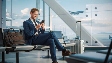 Airport Terminal Flight Wait: Smiling Businessman Uses Smartphone for e-Business, Browsing Internet...