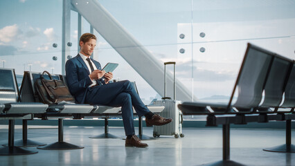 Airport Terminal Flight Wait: Smiling Businessman Uses Digital Tablet Computer for e-Business,...