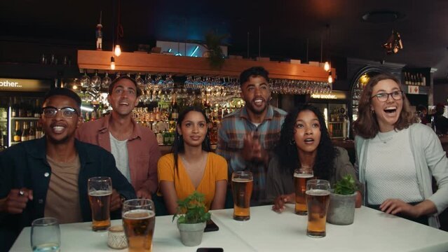diverse group of friends watching sports game in restaurant on the television