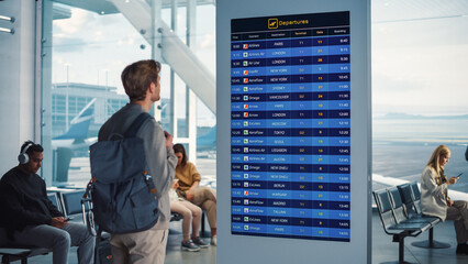 Airport Terminal: Young Man Looking at Arrival and Departure Information Display Looking for His...