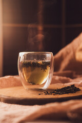 A glass cup of fragrant green tea on a wooden board next to scattered dry tea. steam over a hot drink. Brew tea.