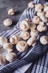 Fresh white champignons on a kitchen towel on a gray background. Kitchen, cooking, recipes. Mushrooms, ingredient.