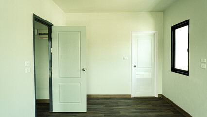 A wooden door in a white room is perpendicular to the right against the background of the entrance wall covered with brown tiles.