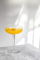 Cocktail glass on white table with hard shadow on the wall . Lemonade or alcohol cocktail minimalist concept.