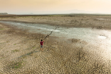 Fototapeta na wymiar Climate Change, Young man on middle of landscape dry river, cracked earth. Metaphor Drought and water crisis.