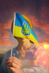 Girl holding ukrainian flag on the background of the burning sky. No war. Support for Ukraine