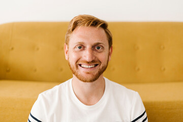 Happy man with red hair in front of sofa at home