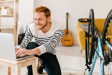 Smiling young man using laptop by bicycle in living room at home