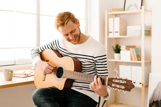 Happy young man playing guitar at home