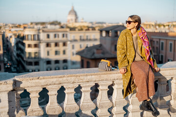 Woman enjoying beautiful morning cityscape of Rome, sitting on the top of famous Spanish steps. Old fashioned woman wearing coat with colorful shawl in hair. Concept of italian lifestyle and travel