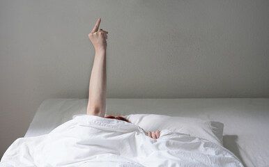 woman flipping the finger while hiding under bed cover