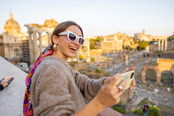Fototapeta na wymiar Woman takes selfie photo on background of the Roman Forum, ruins at the center of Rome on a sunset. Concept of traveling famous landmarks in Italy